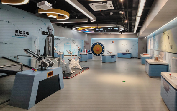 Interactive science exhibits in a modern science museum hall, including bicycle power generator and hands-on physics exhibits.